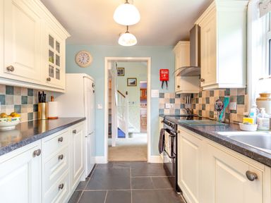 A kitchen with cream cabinets black countertop tiled backsplash and a refrigerator at Westside Cottage in Cardinham near Bodmin