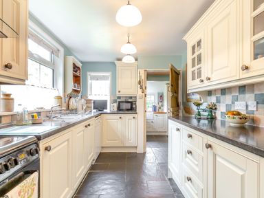 A kitchen with white cabinets a stove a microwave and a bowl of fruit at Westside Cottage in Cardinham near Bodmin