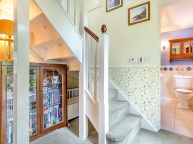 A carpeted staircase with a wooden cabinet under the stairs and a bathroom visible through an open door at Westside Cottage in Cardinham near Bodmin