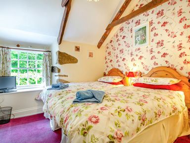A bedroom with two beds with floral bedding and folded towels a small television and floral curtains at Westside Cottage in Cardinham near Bodmin
