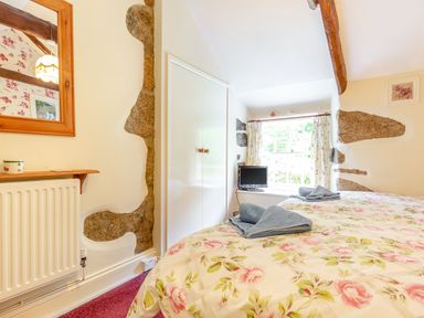A bedroom with twin beds covered in floral bedspreads and blue towels on top near a window with curtains at Westside Cottage in Cardinham near Bodmin
