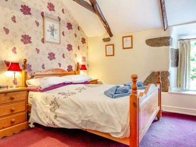 A bedroom with a wooden bed, bedside tables with lamps, floral wallpaper and framed pictures at Westside Cottage in Cardinham near Bodmin