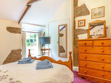 A bedroom with a wooden bed and dresser a window with curtains and a wall-mounted TV at Westside Cottage in Cardinham near Bodmin