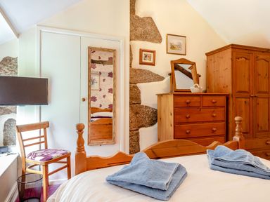A bedroom with wooden bed frame chest of drawers wardrobe chair and wall mirror at Westside Cottage Cardinham near Bodmin