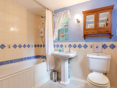 A bathroom with a bathtub and shower curtain a pedestal sink a toilet wooden mirrored cabinet and blue and white tiled walls at Westside Cottage in Cardinham near Bodmin