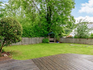 A garden with a wooden deck lawn trees and a wooden fence at Westside Cottage in Cardinham near Bodmin