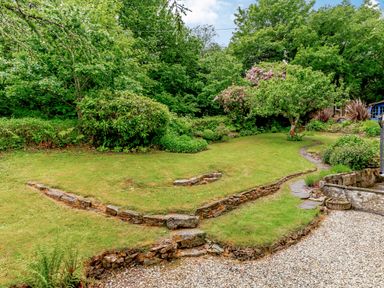 A garden with grass lawn stone pathway and various trees and shrubs at Westside Cottage in Cardinham near Bodmin
