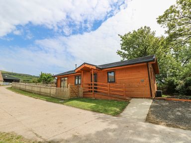 A wooden cabin with a ramp and fenced yard under a partly cloudy sky at Chale Farm Lodge in Chale