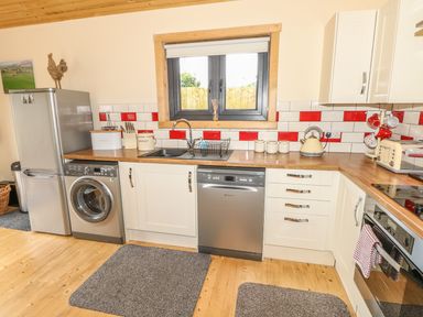 A kitchen with white cabinets wooden countertop and red and white tiled backsplash in Chale Farm Lodge in Chale