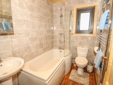 A bathroom with a bathtub shower combination a toilet a sink and a window at Chale Farm Lodge in Chale