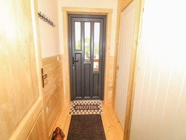 A hallway with a black door at the end a welcome mat a coat hook on the wall and wooden paneling at Chale Farm Lodge in Chale