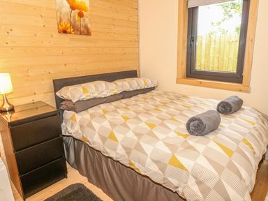 A bedroom with a double bed and a window next to it with a bedside table and lamp at Chale Farm Lodge in Chale