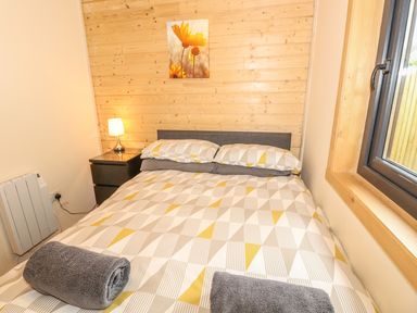 A bedroom with a double bed two rolled towels bedside table with lamp and window at Chale Farm Lodge in Chale