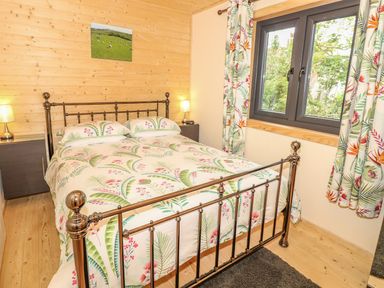 A bedroom with a metal bed frame floral bedding two bedside tables with lamps a window with floral curtains and a photograph on a wooden wall at Chale Farm Lodge in Chale