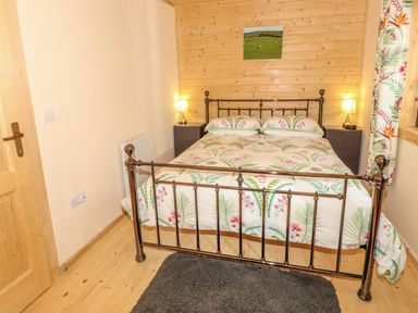 A bedroom with a metal frame bed floral bedding two bedside tables with lamps wooden walls curtains and a small framed picture at Chale Farm Lodge in Chale