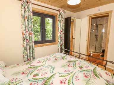 A bedroom with a bed covered in floral bedding next to a window with matching curtains and a door leading to a bathroom at Chale Farm Lodge in Chale