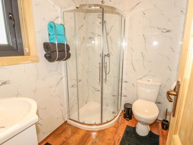 A bathroom with a corner glass shower, a toilet, towels on a rack, and wooden flooring at Chale Farm Lodge in Chale