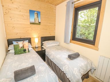 A small bedroom with two single beds a nightstand with a lamp a window and wooden paneling on one wall at Chale Farm Lodge in Chale