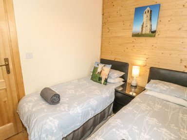 A bedroom with two single beds a bedside table with a lamp and a door at Chale Farm Lodge in Chale