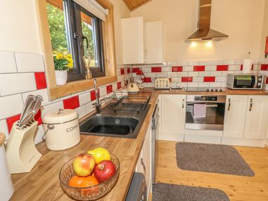 A kitchen with wooden countertops white cabinets and red and white tiled backsplash at Chale Farm Lodge in Chale