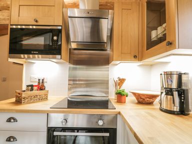 A kitchen with wooden cabinets a microwave oven stovetop oven wooden utensils potted plant bowl and coffee maker at Heron Lodge in North Kessock