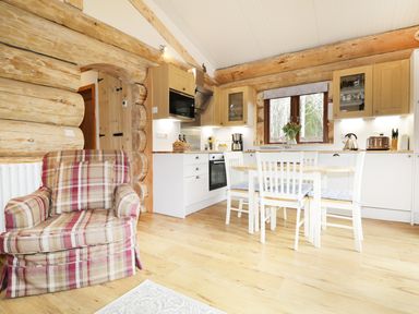A kitchen and dining area with wooden cabinets a white dining table with chairs and a plaid armchair at Heron Lodge in North Kessock