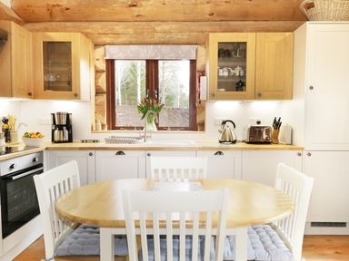 A kitchen with wooden cabinets a round dining table white chairs and a window with flowers on the windowsill at Heron Lodge in North Kessock