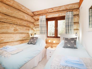 A bedroom with two single beds a window and wooden log walls at Heron Lodge in North Kessock