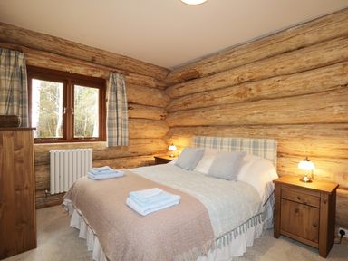 A bedroom with a double bed two bedside tables with lamps a wooden dresser and a window with curtains at Heron Lodge in North Kessock
