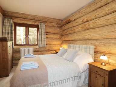 A bedroom with a bed side tables lamps and wooden dresser in a log cabin at Heron Lodge in North Kessock