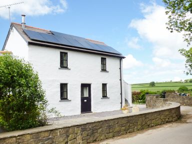 A white two-story house with solar panels on the roof and black framed windows behind a stone wall in a rural area at The Old Granary in Spittal