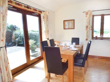 A dining room with a wooden table set with white crockery and six black chairs at The Old Granary in Spittal