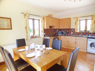 A kitchen and dining area with a wooden table set with cups and plates and black chairs at The Old Granary in Spittal
