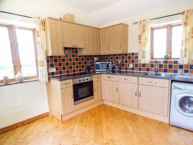 A kitchen with wooden cabinets tiled backsplash and wooden floor at The Old Granary in Spittal