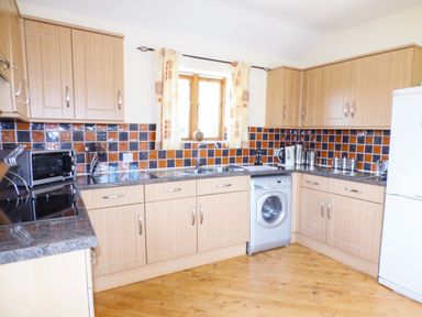 A kitchen with wooden cabinets a washing machine a microwave and a refrigerator at The Old Granary in Spittal