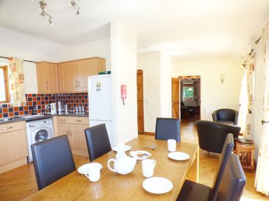 A kitchen and dining area with wooden cabinets a refrigerator a washing machine and a wooden table with chairs at The Old Granary in Spittal