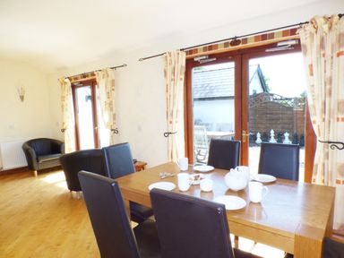 A dining area with wooden table and black chairs near glass doors leading to a patio with outdoor furniture at The Old Granary in Spittal