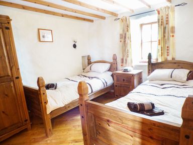 A bedroom with two single wooden beds a wooden wardrobe and a wooden nightstand under a window at The Old Granary in Spittal