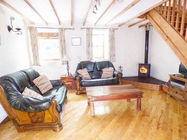 A living room with leather sofas a wooden coffee table and a wood burning stove at The Old Granary in Spittal