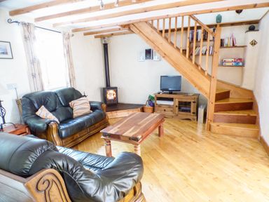 A living room with leather sofas a wooden coffee table a wood burning stove a wooden staircase and a small television at The Old Granary in Spittal