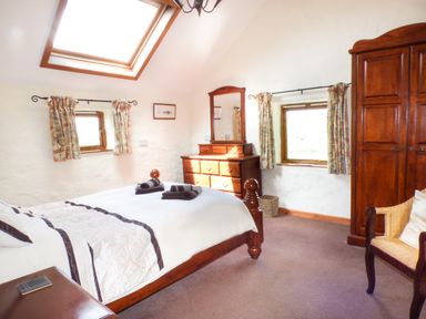 A bedroom with a wooden bed chest of drawers wardrobe and chair at The Old Granary in Spittal