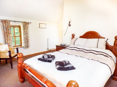 A bedroom with a wooden bed, bedside table, armchair, window with curtains at The Old Granary in Spittal