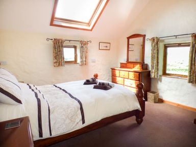 A bedroom with a bed, dresser with mirror, and three windows at The Old Granary in Spittal