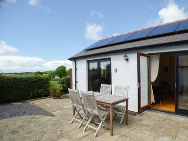 An outdoor patio area with a wooden table and chairs next to a white building with solar panels on the roof at The Old Granary in Spittal