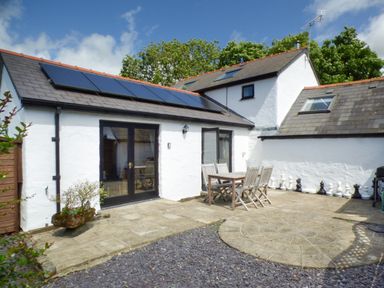A patio area with wooden table and chairs outside a white building with solar panels on the roof at The Old Granary in Spittal