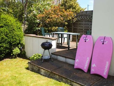 A garden patio with a table and chairs a small barbecue and two pink bodyboards at Pendeen in Wadebridge