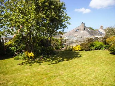 A garden with grass, trees, shrubs, and houses in the background at Pendeen in Wadebridge