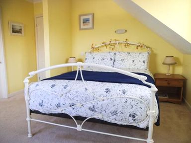A bedroom with a white metal bed frame decorated with string lights a wooden nightstand with a lamp and yellow walls at Pendeen in Wadebridge