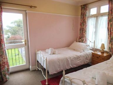 A bedroom with two single beds a wooden nightstand with a lamp and floral curtains at Pendeen in Wadebridge