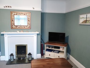A room with a fireplace decorated with shells and lanterns and a television on a wooden cabinet at Pendeen in Wadebridge